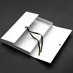 an open white box with a black ribbon on the bottom and inside, sitting on a dark surface