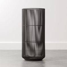 a tall black vase sitting on top of a cement floor next to a white wall