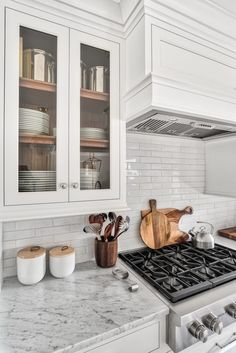 a kitchen with white cabinets and marble counter tops is pictured in this image, there are wooden utensils on the stove