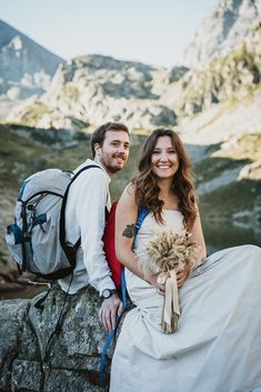 a man and woman are sitting on a rock in front of some mountains, one is holding a bouquet