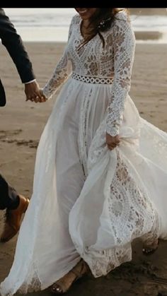 a man and woman are walking on the beach holding hands while dressed in wedding attire