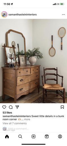 a wooden dresser sitting in front of a mirror next to a chair and wall hangings