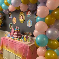 a table topped with lots of balloons next to a wall filled with pictures and cake