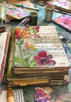 an altered book with flowers and music notes on it sitting on a table next to paintbrushes