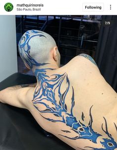 a man with blue ink on his back and shoulder sitting in front of a mirror