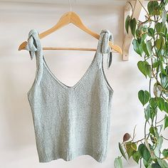 a cropped top hanging on a wooden hanger next to a potted plant