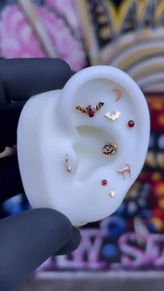 a person is holding an earring in front of a wall with colorful designs on it