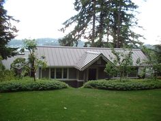 a house in the middle of some trees and bushes with a metal roof on it