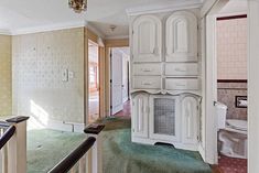 an empty room with white cabinets and green carpeted stairs leading up to the second floor