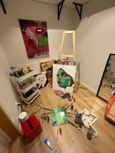 an art studio with various pieces of artwork on the floor, including a painting and easel