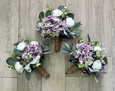 three bridal bouquets with purple and white flowers arranged on the floor in a circle