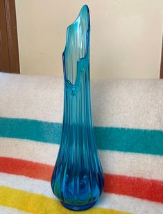 a blue glass vase sitting on top of a striped table cloth next to a wall