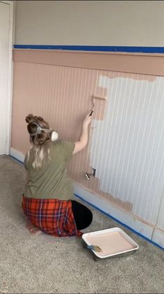 a woman sitting on the floor painting a wall