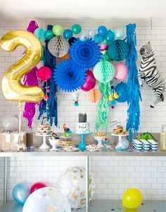 a table with balloons, streamers and confetti on it in front of a white brick wall