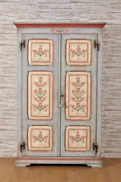 an old blue cabinet with flowers painted on the front and sides, against a brick wall