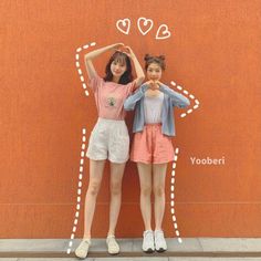 two young women standing next to each other in front of a wall with hearts drawn on it