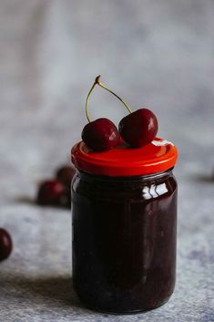 two cherries sit on top of a jar of jam