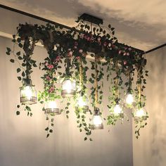 a bunch of plants that are hanging from the ceiling in front of a wall with lights on it