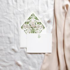 a white envelope with a green and white floral design on it next to a pink satin fabric