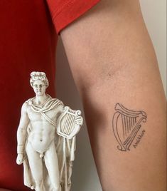 a small tattoo on the arm of a man with a harp and statue behind it