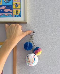 a hand is holding two pom poms on a keychain hanging from a wall