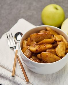 a bowl filled with apples and cinnamon on top of a white napkin next to two forks