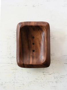 a wooden bowl sitting on top of a white table next to a black object with holes in it