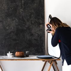 a woman taking a photo with her camera next to a blackboard and cake on a table