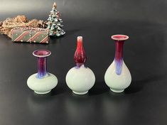 three small vases sitting on top of a black table next to a christmas tree