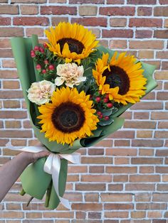 a bouquet of sunflowers is being held by someone's hand against a brick wall