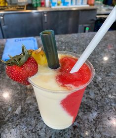 a drink in a glass with strawberries on the rim and a plastic straw sticking out of it