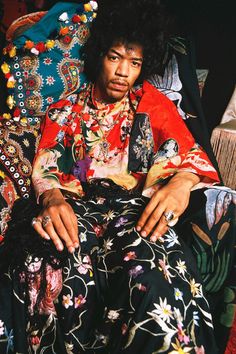 a man sitting on top of a bed covered in lots of colorful clothing and jewelry