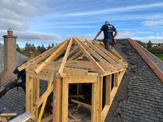 a man standing on top of a roof next to a building under construction with wood framing