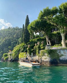 a small boat is on the water in front of a hillside with trees and bushes