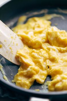 scrambled eggs being cooked in a skillet with a spatula on the side,