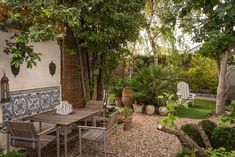 an outdoor dining area with wooden table and chairs in the middle of it, surrounded by greenery