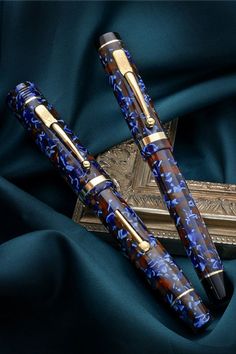 two fountain pens sitting on top of a blue cloth