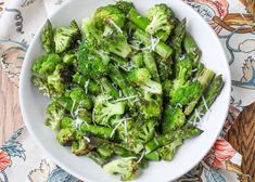 a white bowl filled with broccoli covered in parmesan cheese on top of a table