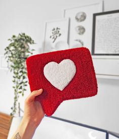 a person holding up a red and white heart shaped pillow