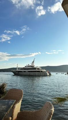 a large boat is in the water near some wicker chairs and an outdoor dining table