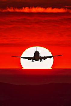 an airplane is flying in front of the setting sun