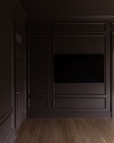 an empty room with wood floors and dark walls, has a flat screen tv on the wall