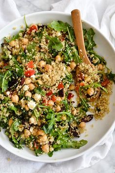 a white bowl filled with lots of food on top of a table next to a wooden spoon