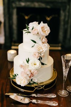 a wedding cake with white flowers and greenery sits on a table next to silverware