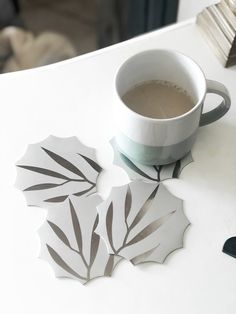 a cup of coffee sitting on top of a white table next to two leaf shaped coasters