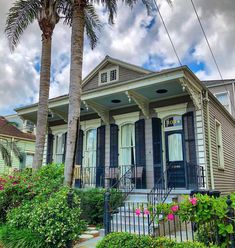 a small house with palm trees in front of it and flowers on the side walk