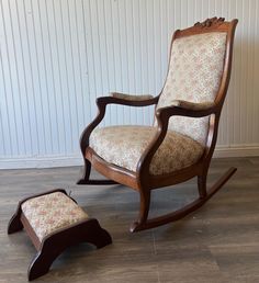 a wooden rocking chair with footstool in front of a white wall and wood floor