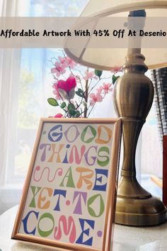 a table with a lamp and a painting on it that says good things are coming