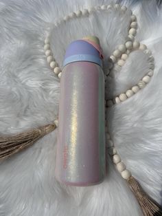 a pink and blue water bottle laying on top of a white fur covered floor next to a beaded necklace