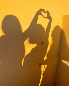 the shadow of a woman making a heart sign with her hand on a yellow wall